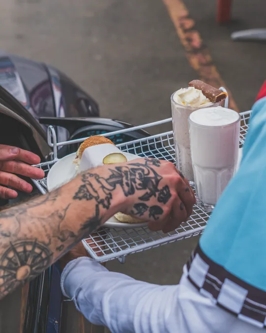 A customer receiving food and milkshakes at a car
