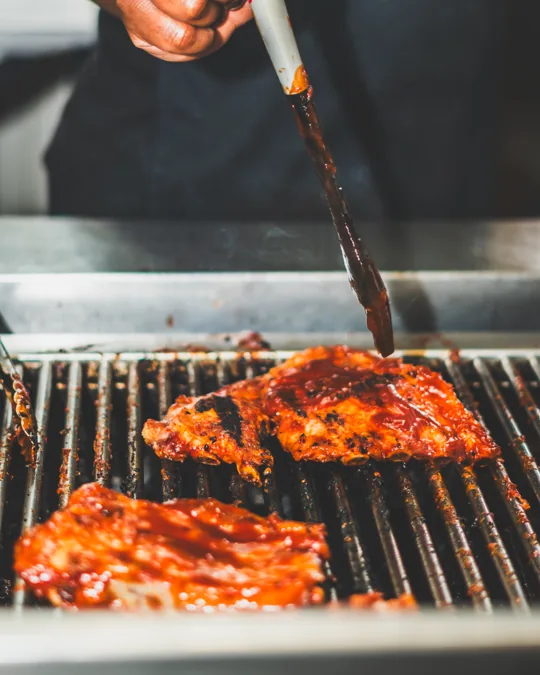 Meat being brushed with sauce on the grill