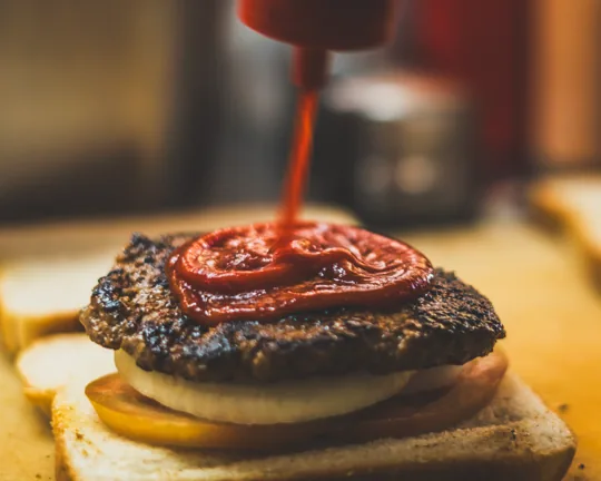 A burger patty being topped with sauce
